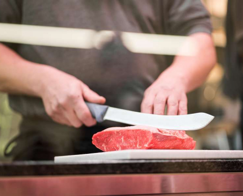 Person schneidet Fleisch mit Messer