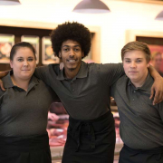 Drei Personen Arm in Arm vor einer Metzgertheke